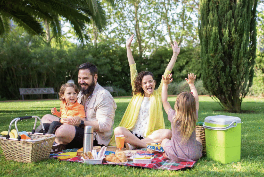 2 parents and 2 kids site on a picnic blanket enjoying a picnic in the park